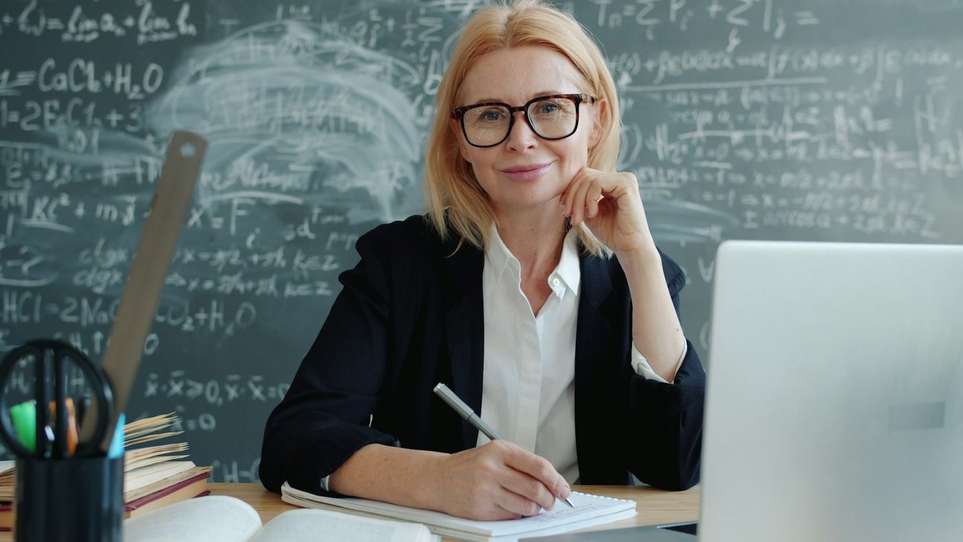 A teacher smiling at her desk with a laptop